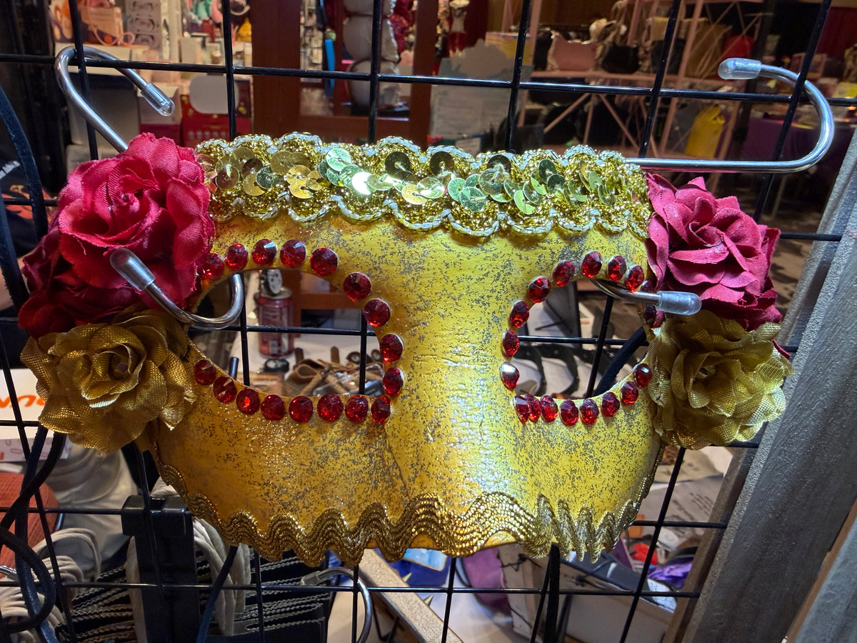 Decorative metallic gold mask with red embellishments and pink flowers on a stand.