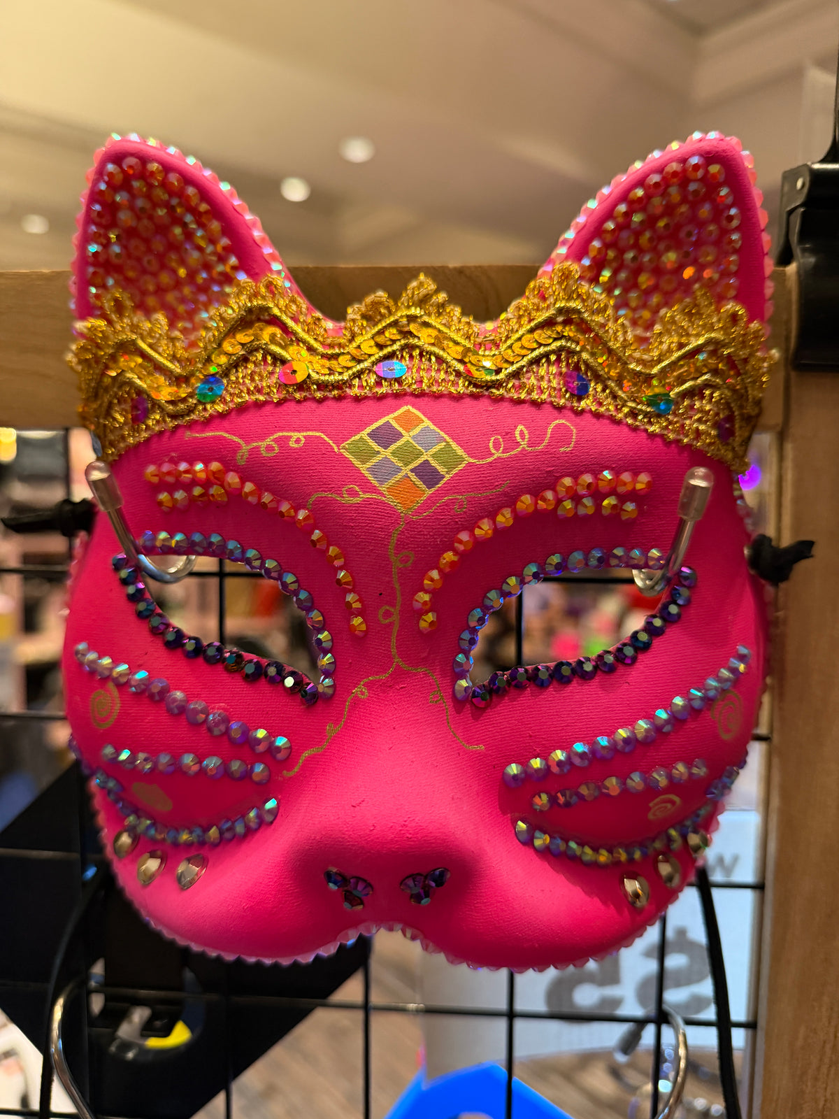 Pink cat mask with gold accents and colorful stones on a stand.